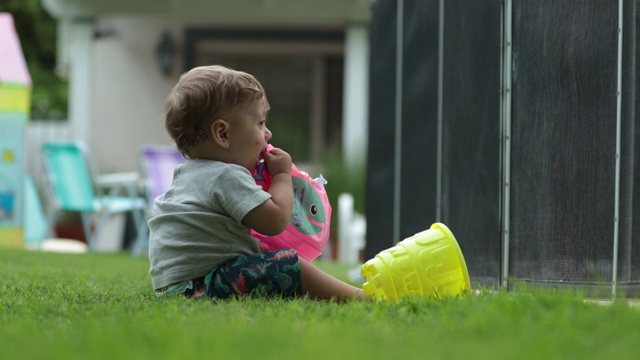 蹒跚学步的婴儿在后院户外把物体放进嘴里视频素材