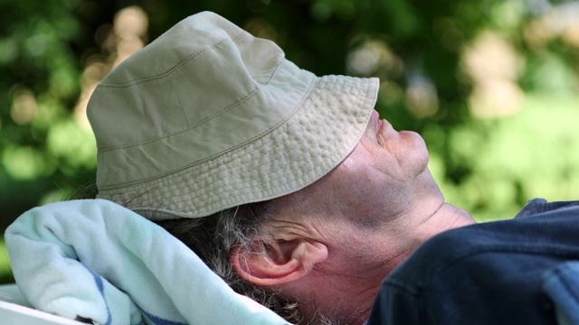 一位老人戴着帽子在外面打盹。在户外睡觉的老年人视频下载