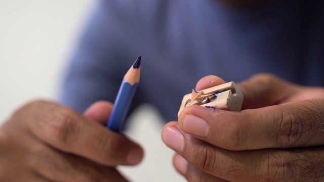 教育的概念。靠近男性的手正在削蓝铅笔与卷笔刀。视频下载