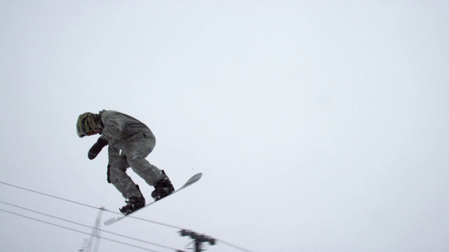 在完整的冬季装备滑雪板完成一个“背面360”在一个森林和滑雪电梯在背景Eldora滑雪度假村附近博尔德，科罗拉多州在一个下雪，阴天的慢动作拍摄视频素材