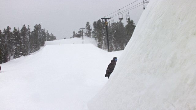 在科罗拉多州博尔德附近的埃尔多拉滑雪度假村在一个下雪的，阴天完成一个“开关540陈腐抓取”的跳跃技巧视频素材