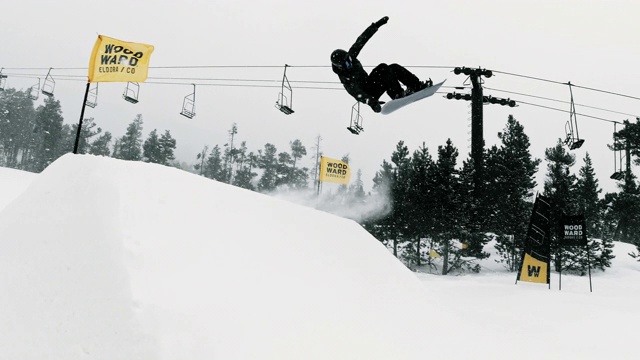 完成一个“开关540尾巴抓斗”在一个跳跃与森林和滑雪跳跃的背景在埃尔多拉滑雪度假村附近的博尔德，科罗拉多州在一个下雪的，阴天的诡计视频下载