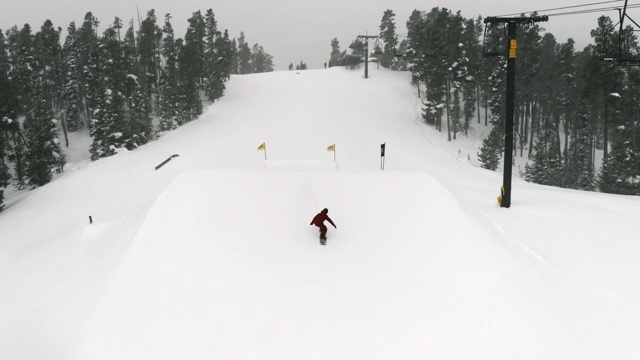 慢动作，无人机拍摄的滑雪板在完整的冬季装备完成一个“背面180个瓜”的技巧与森林和滑雪升降机在背景在科罗拉多州博尔德附近的埃尔多拉滑雪度假村在一个下雪，阴天视频素材