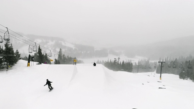 慢动作，无人机拍摄的滑雪板在完整的冬季装备完成一个“背面360”技巧与森林和滑雪升降机在背景在科罗拉多州博尔德附近的埃尔多拉滑雪度假村在一个下雪，阴天视频素材