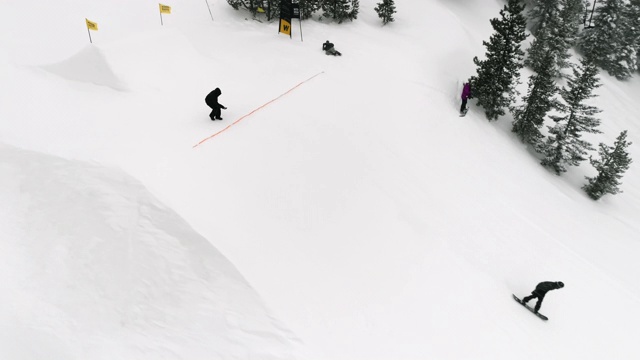 在科罗拉多州博尔德附近的埃尔多拉滑雪度假村，在一个下雪的，阴天完成一个跳跃与森林和滑雪缆车的“开关前侧540”把戏视频素材