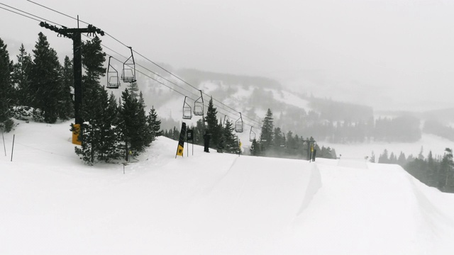 在科罗拉多州博尔德附近的埃尔多拉滑雪度假村，在一个下雪的，阴天完成一个跳跃与森林和滑雪缆车的“开关背面540尾巴抓取”的技巧视频素材
