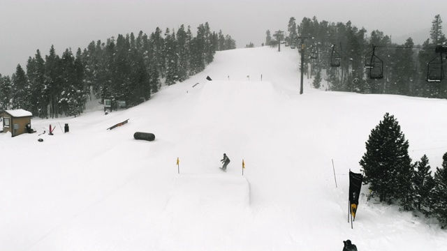 在科罗拉多州博尔德附近的埃尔多拉滑雪度假村，在一个下雪的，阴天的背景下完成一个跳跃与森林和滑雪升降机的“静音抓取”技巧视频素材