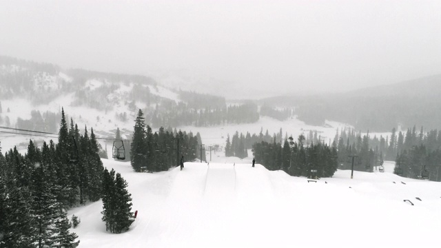 在科罗拉多州博尔德附近的埃尔多拉滑雪度假村，在一个下雪的阴天，完成一个跳跃与森林和滑雪缆车的“开关前540火箭抓取”的技巧视频素材