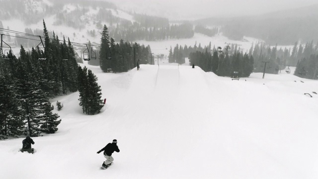 慢动作，无人机拍摄的滑雪板在完整的冬季装备完成一个“前侧540 Off脚趾”的技巧与森林和滑雪缆车在背景在科罗拉多州博尔德附近的埃尔多拉滑雪度假村在一个下雪，阴天视频素材