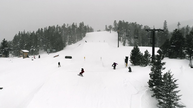 慢动作，无人机拍摄的滑雪板在完整的冬季装备完成一个“背面540尾巴抓取”在跳跃与森林和滑雪升降机在背景在科罗拉多州博尔德附近的埃尔多拉滑雪度假村在一个下雪，阴天视频素材