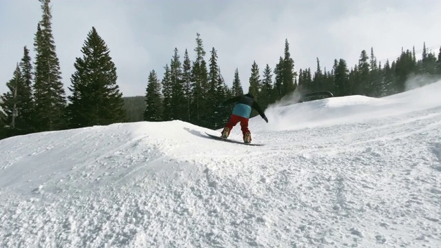 一个滑雪板在完整的冬季装备完成多个技巧(“5050，”“正面滑板270，”缺口正面Lipslide，“背面360鼻黄油，”和“背面5050”)在一个跳跃和特技轨道与森林和滑雪跳跃在背景在埃尔朵拉Sk视频下载