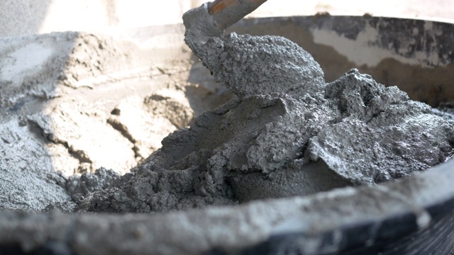 建筑工人或抹灰工人在建筑工地用铲斗舀拌混凝土。建筑的概念。视频下载