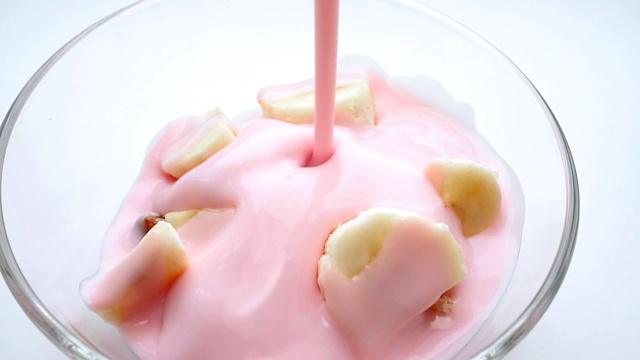 特写镜头中，将草莓酸奶和香蕉一起倒入格兰诺拉麦片中。健康的饮食早餐视频素材