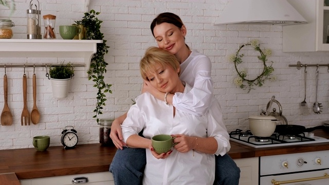 一个快乐的老母亲和女儿在厨房里，她们在喝茶。视频素材