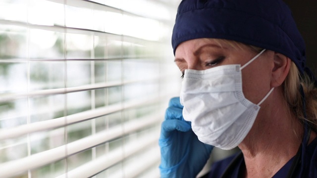 压力大的医生或护士在窗户上拿着医用口罩。视频素材