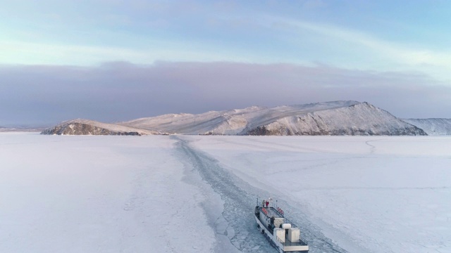 空中的小船在贝加尔湖的冰面上漂浮。无人机跟踪一艘在冰上移动的破冰船视频素材