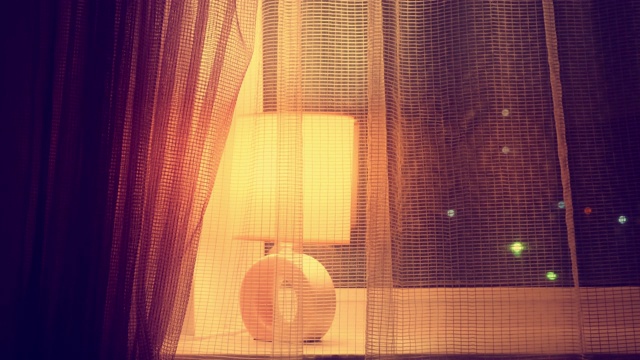 一个女人拿着窗帘和台灯站在夜晚的窗前。女在窗边伤心视频下载