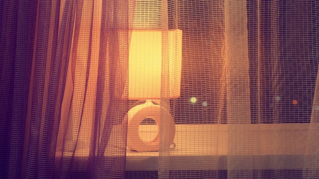夜晚挂着窗帘的窗户上的灯。窗户上的台灯发出的光视频下载