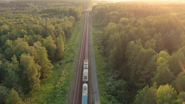 鸟瞰图:火车在夏天的乡村景象。火车在日出时穿过乡村。火车沿着美丽的夏日森林带行驶。美好的阳光。视频素材