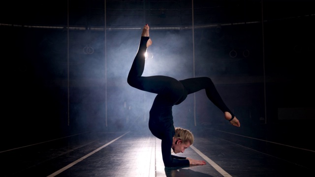 女体操运动员在黑暗的舞蹈工作室里表演的剪影。灵活的女人视频下载