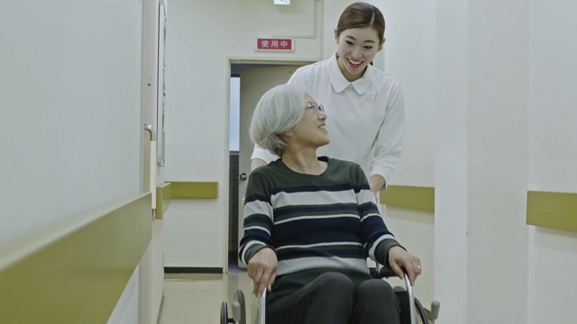 日本护士用轮椅推病人走过医院走廊视频素材