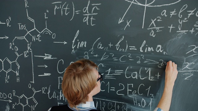 聪明的年轻人在课堂上用粉笔在黑板上写数学方程视频素材