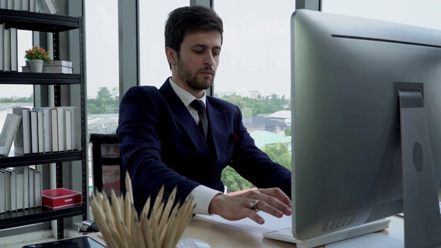 一位穿着黑色西装的年轻商人正在工作场所使用电脑。视频下载