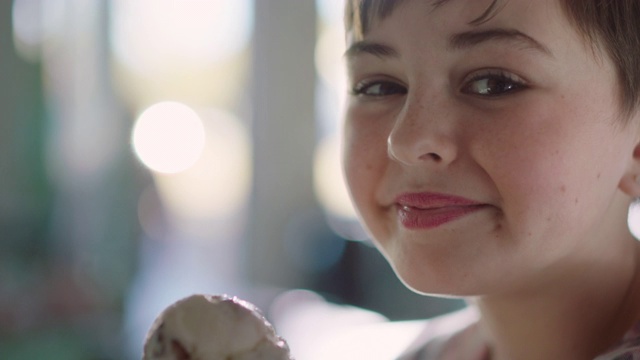一个在冰淇淋店吃冰淇淋的女孩对着镜头微笑的肖像视频下载