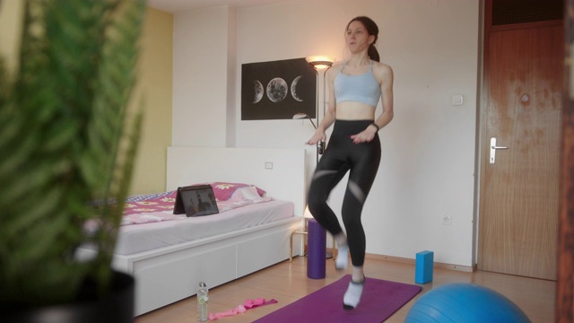 被隔离的年轻女性在平板电脑旁边做家庭运动，视频锻炼视频下载