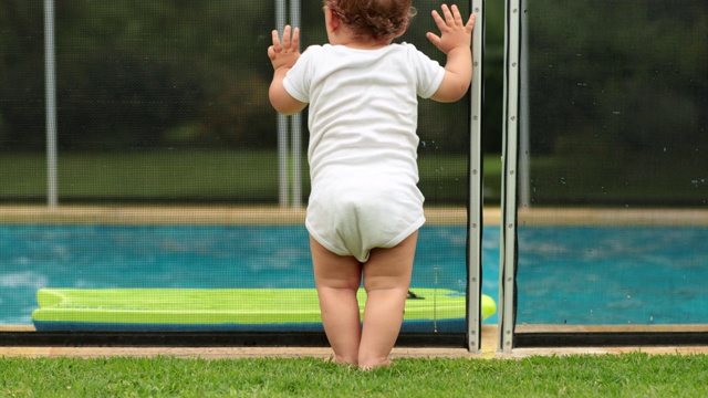 宝宝靠在游泳池围栏上安全。婴儿在前景，而孩子在后台玩视频素材