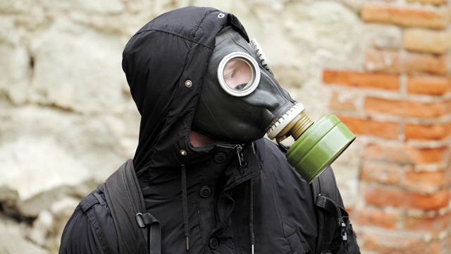 画像是一个穿着黑衣戴着防毒面具的流浪男子穿过一座废弃的建筑。后启示录世界。跟踪者的概念，核战争或化学战争后的幸存者。关闭了。视频下载