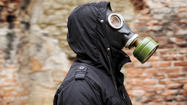 画像是一个穿着黑衣戴着防毒面具的流浪男子穿过一座废弃的建筑。后启示录世界。跟踪者的概念，核战争或化学战争后的幸存者。近距离视频下载