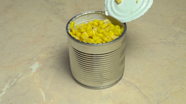 一个女人的手打开了一个铁罐的玉米罐头。视频下载