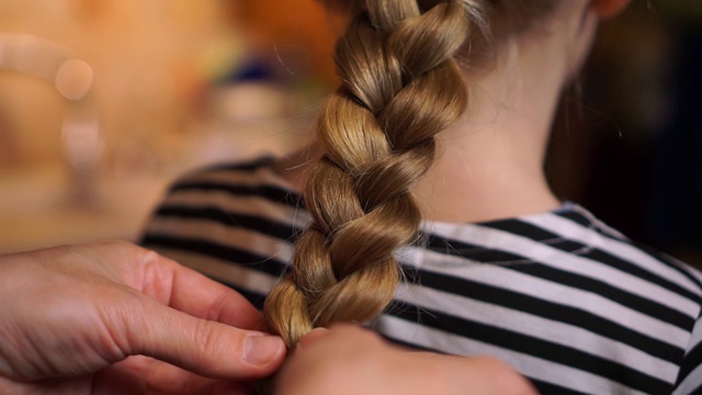 母亲编辫子与编织的发型为女儿孩子长金发女孩穿着条纹裙在厨房舒适的家。妈妈关心孩子视频下载