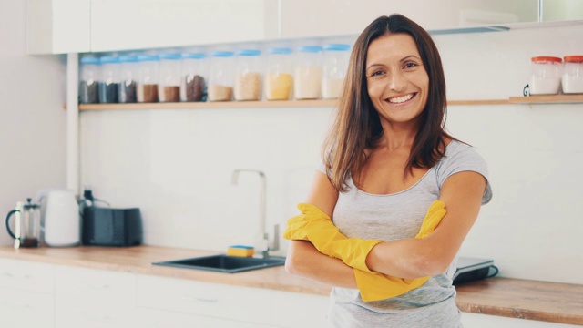 家务活。漂亮的女人，戴着黄色的酒吧手套，是真诚的微笑，在厨房的背景。副本的空间。关闭了。4 k。视频下载