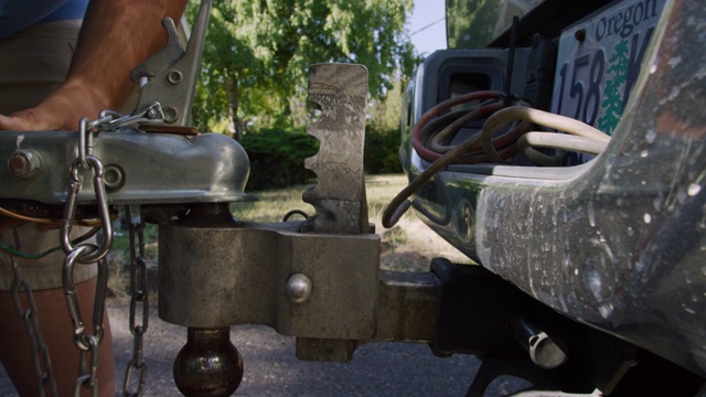 一个西班牙裔男子的手附上一个拖车耦合器与一个闩在球栓在他的车辆在一个阳光明媚的日子视频下载