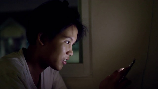 一个亚洲女人晚上在家里用智能手机视频下载