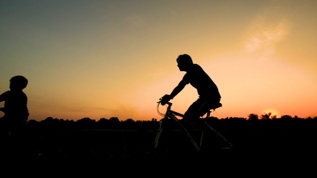 剪影父亲和孩子在夕阳下骑自行车视频下载