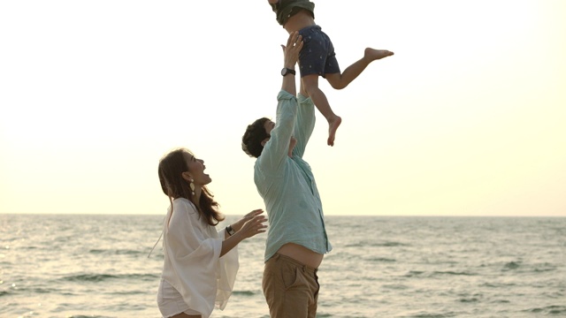 慢镜头:日落时分，快乐的亚洲家庭在海滩上玩耍，父亲把小男孩抛向空中。视频素材