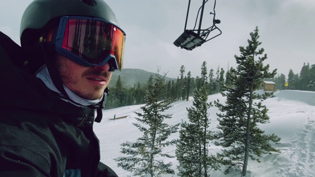 一个阳光明媚的日子，在科罗拉多州博尔德附近的埃尔朵拉滑雪度假村，一名20多岁的男性滑雪爱好者乘坐滑雪缆车视频下载