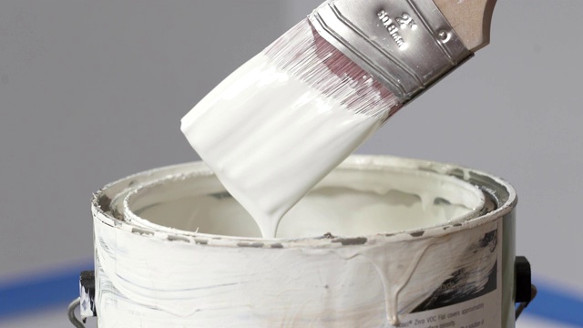 一名油漆工将画笔浸入装有白漆的桶中。颜料从画笔滴进桶里视频下载