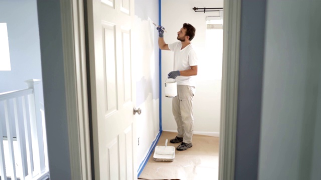 画家在家里粉刷墙壁，用油漆刷和白色油漆。室内装修。4 k视频素材