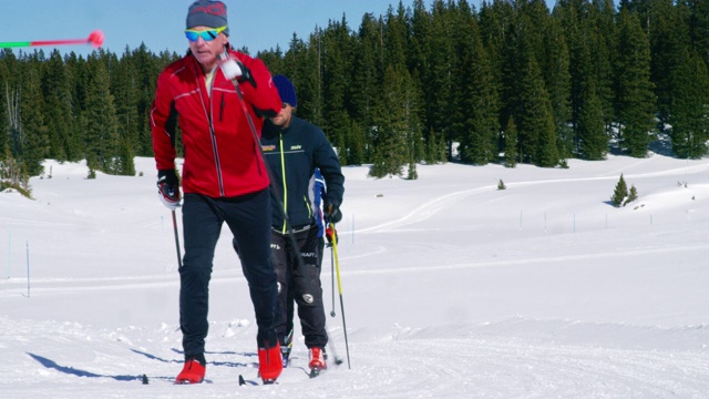 一组四个成年人越野滑雪在一条线在一个阳光明媚，冬日在科罗拉多的慢动作镜头视频下载