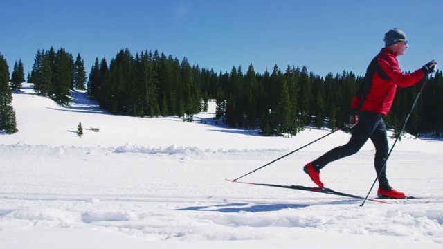 慢动作拍摄的一个男人在他的五十多岁越野滑雪在山在一个阳光明媚，冬日在科罗拉多州视频下载
