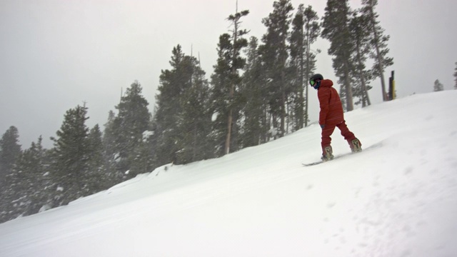 慢动作拍摄的一个滑雪板穿着完整的冬季装备单板滑雪在埃尔多拉滑雪度假村附近的博尔德，科罗拉多州被滑雪电梯和森林在一个下雪，阴天视频素材