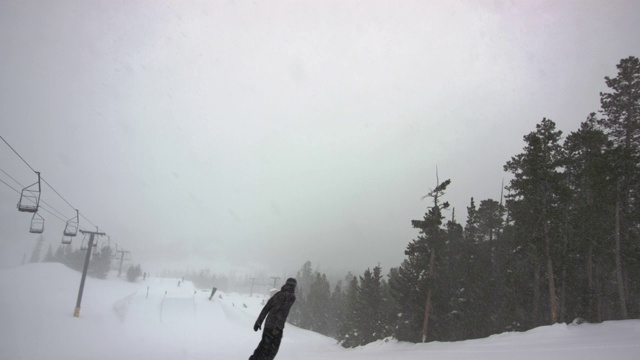 慢动作拍摄的一个滑雪板穿着完整的冬季装备单板滑雪在埃尔多拉滑雪度假村附近的博尔德，科罗拉多州被滑雪电梯和森林在一个下雪，阴天视频素材