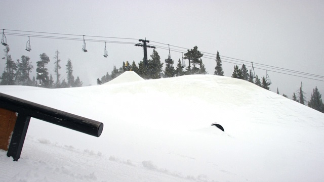完整的冬季装备滑雪板完成一个“背面540”技巧与森林和滑雪缆车在背景在科罗拉多州博尔德附近的埃尔多拉滑雪度假村在一个下雪的，阴天从远处视频素材