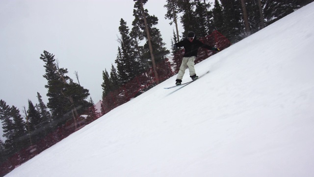 慢动作拍摄的滑雪板穿着完整的冬季装备停止在滑雪跑后做了一个“BS黄油”的伎俩被森林包围在博尔德附近的埃尔朵拉滑雪度假村，科罗拉多州在一个下雪的，阴天，雪遍布周围视频素材
