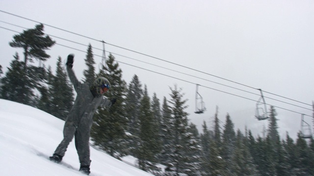 在科罗拉多州博尔德附近的埃尔多拉滑雪度假村，一名摄影师躺下并拍下了一名滑雪板在完整的冬季装备完成一个“后空翻Tucknee”跳跃技巧与森林和滑雪缆车为背景的慢动作镜头，视频素材