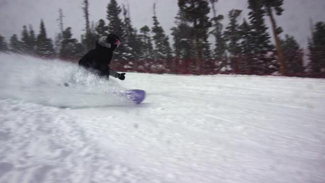 慢动作拍摄的滑雪板穿着完整的冬季齿轮雕刻在滑雪跑和喷涂雪在摄像机周围的埃尔多拉滑雪度假村附近的博尔德，科罗拉多州在一个下雪的，阴天，雪喷雾周围视频素材